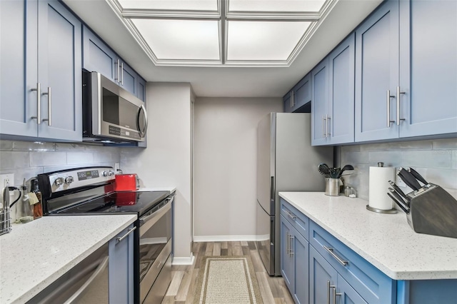 kitchen with appliances with stainless steel finishes, tasteful backsplash, light stone countertops, blue cabinetry, and light wood-type flooring