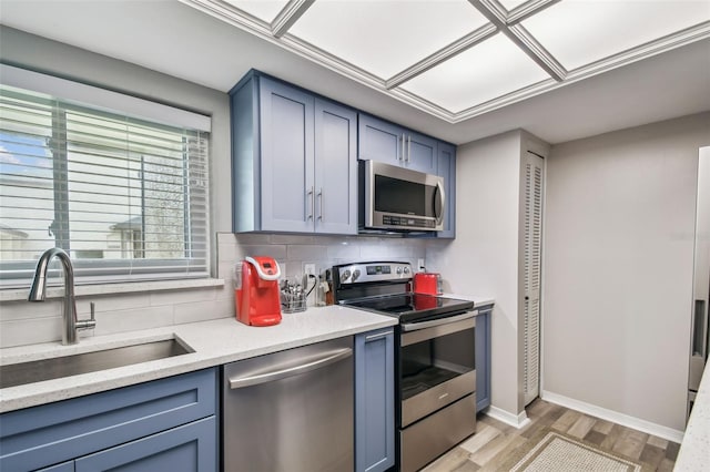 kitchen featuring blue cabinetry, sink, tasteful backsplash, stainless steel appliances, and light hardwood / wood-style floors