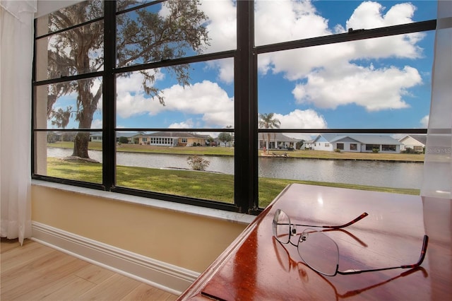 interior space with wood finished floors, a water view, baseboards, and a residential view