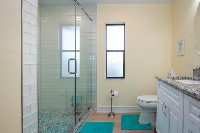 bathroom featuring toilet, wood finished floors, vanity, a shower stall, and baseboards