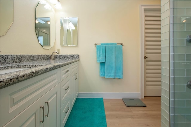 bathroom with a sink, wood finished floors, double vanity, baseboards, and a tile shower
