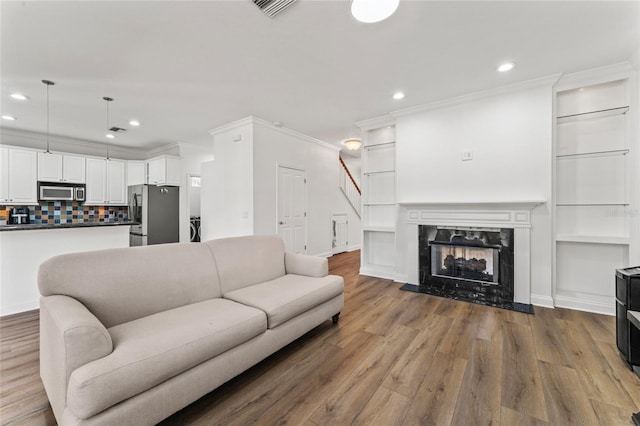 living room featuring built in shelves, ornamental molding, wood-type flooring, and a fireplace