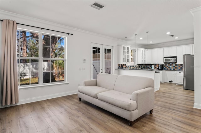 living room featuring french doors, crown molding, and light wood-type flooring