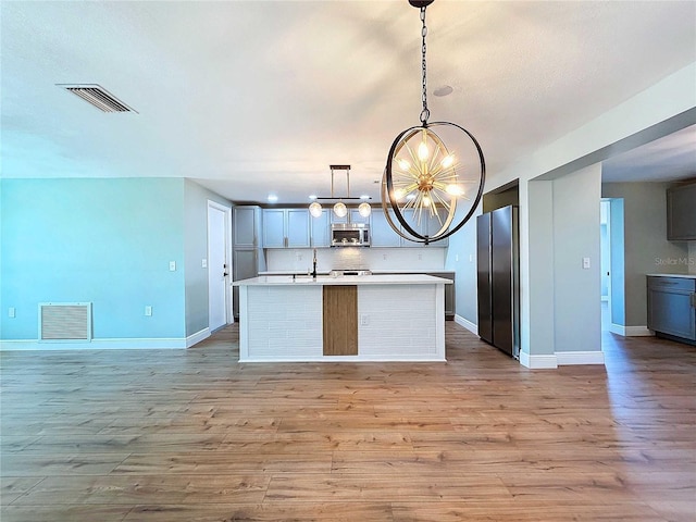 kitchen featuring an inviting chandelier, hanging light fixtures, light wood-type flooring, appliances with stainless steel finishes, and a kitchen island with sink