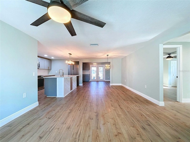 unfurnished living room featuring french doors, sink, a textured ceiling, light hardwood / wood-style floors, and ceiling fan with notable chandelier