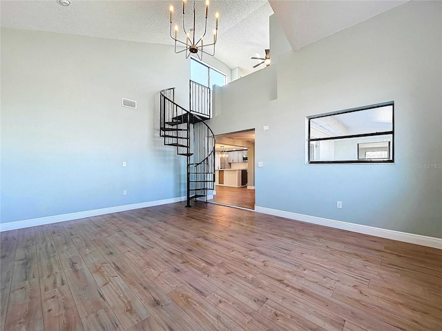 unfurnished living room featuring a high ceiling, ceiling fan with notable chandelier, a textured ceiling, and light hardwood / wood-style flooring