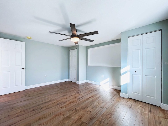 unfurnished bedroom with hardwood / wood-style flooring, ceiling fan, and multiple closets