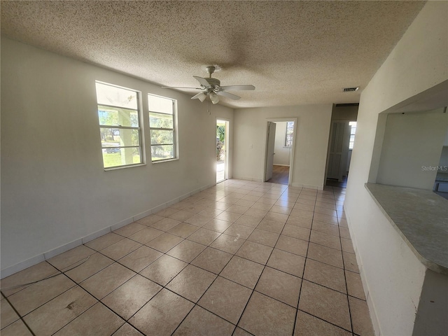 spare room featuring light tile patterned floors, ceiling fan, a textured ceiling, and a wealth of natural light