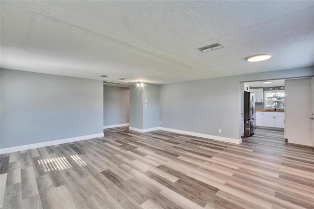 spare room with a textured ceiling, light wood-style flooring, a sink, visible vents, and baseboards