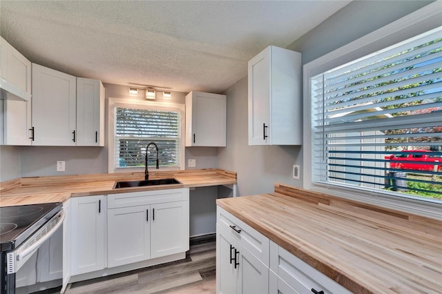 kitchen featuring butcher block countertops, a sink, white cabinetry, and stainless steel electric stove