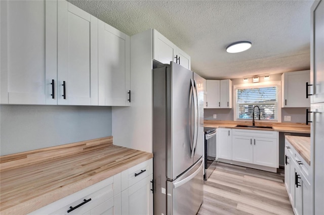 kitchen featuring stainless steel appliances, butcher block countertops, a sink, and white cabinets