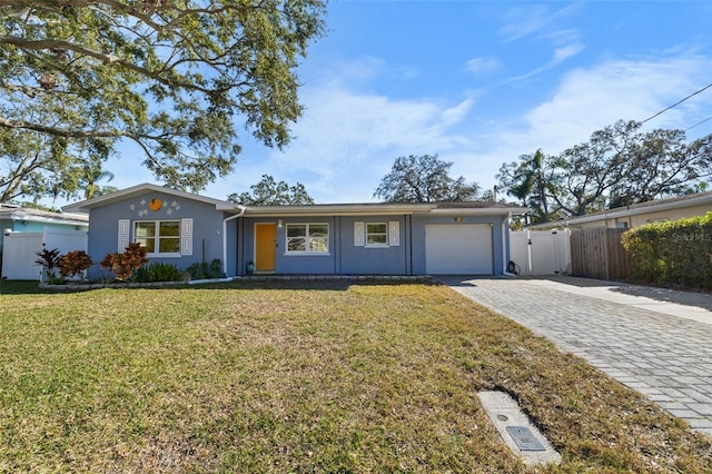 ranch-style house featuring decorative driveway, stucco siding, an attached garage, fence, and a front lawn