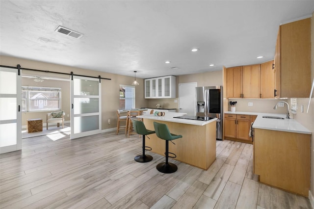 kitchen featuring a barn door, a kitchen island, visible vents, light countertops, and stainless steel refrigerator with ice dispenser