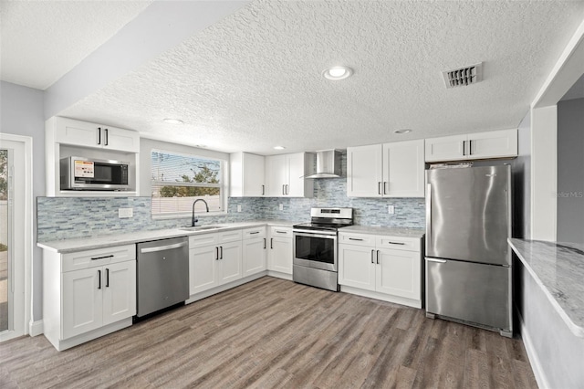 kitchen featuring stainless steel appliances, white cabinetry, sink, and wall chimney range hood