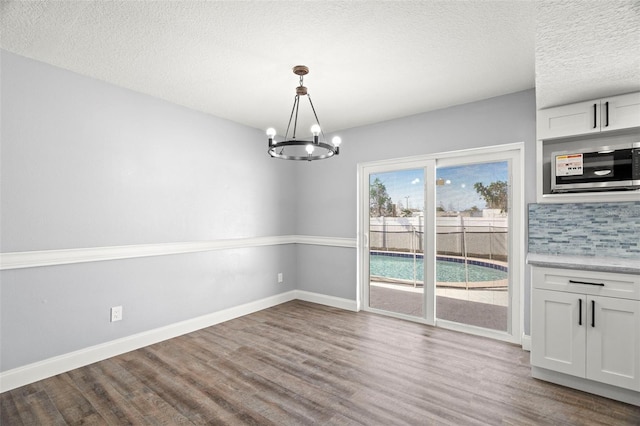 unfurnished dining area with hardwood / wood-style floors, a notable chandelier, and a textured ceiling