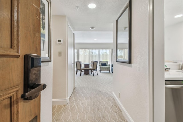 hallway with light colored carpet and a textured ceiling