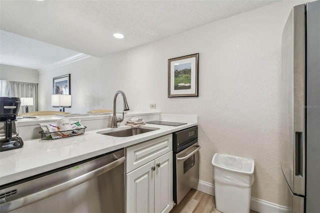 kitchen featuring white cabinetry, sink, light wood-type flooring, stainless steel appliances, and a textured ceiling