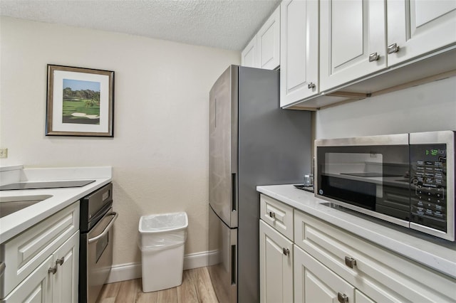 kitchen with stainless steel appliances, a textured ceiling, light hardwood / wood-style flooring, and white cabinets