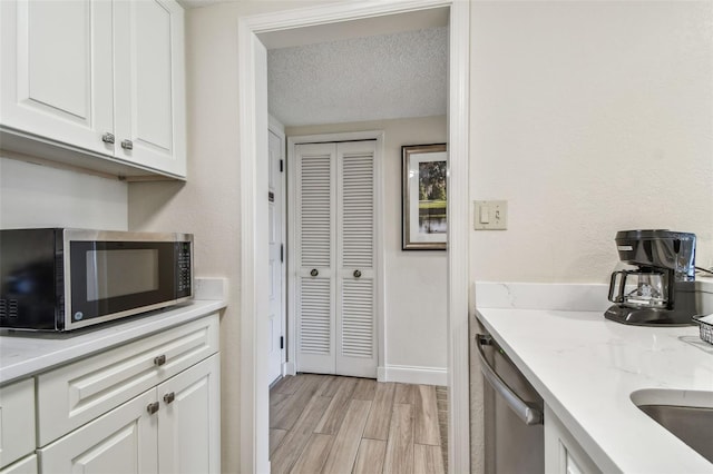 kitchen featuring stainless steel appliances, white cabinets, a textured ceiling, and light hardwood / wood-style flooring