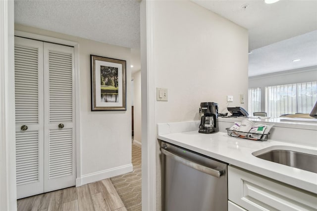 kitchen featuring sink, white cabinetry, a textured ceiling, light wood-type flooring, and stainless steel dishwasher