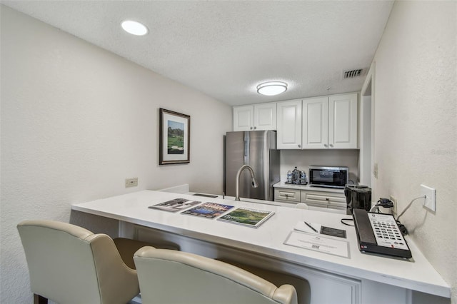 kitchen with a breakfast bar, white cabinetry, a textured ceiling, stainless steel refrigerator, and kitchen peninsula