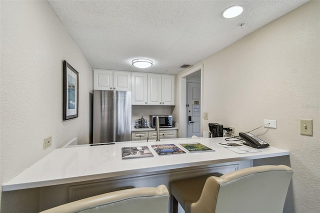 kitchen featuring a kitchen bar, a textured ceiling, kitchen peninsula, stainless steel appliances, and white cabinets