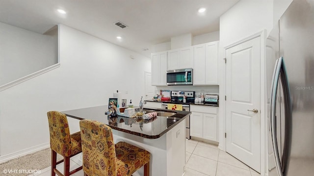 kitchen with appliances with stainless steel finishes, sink, white cabinets, a kitchen bar, and light tile patterned floors