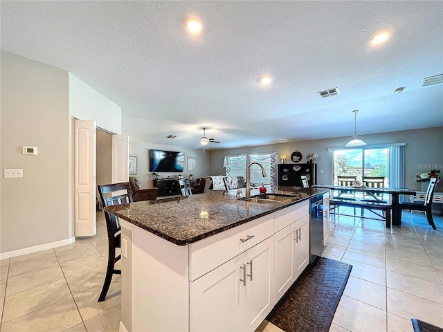 kitchen featuring sink, a breakfast bar, a kitchen island with sink, white cabinets, and decorative light fixtures