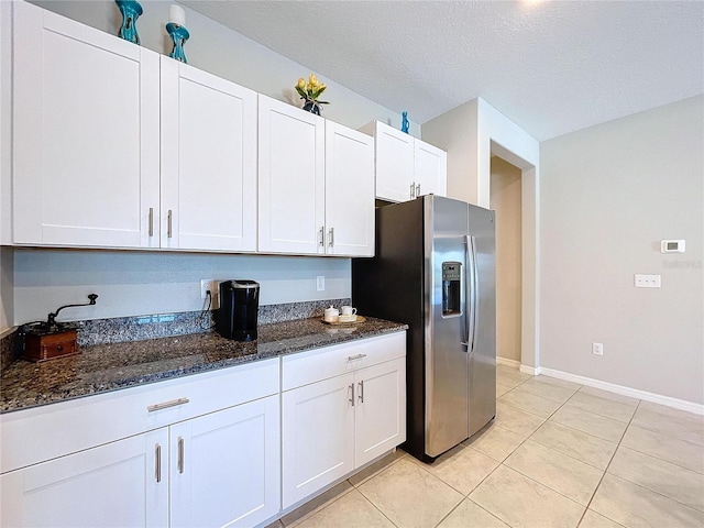 kitchen with stainless steel refrigerator with ice dispenser, white cabinetry, dark stone counters, and light tile patterned floors