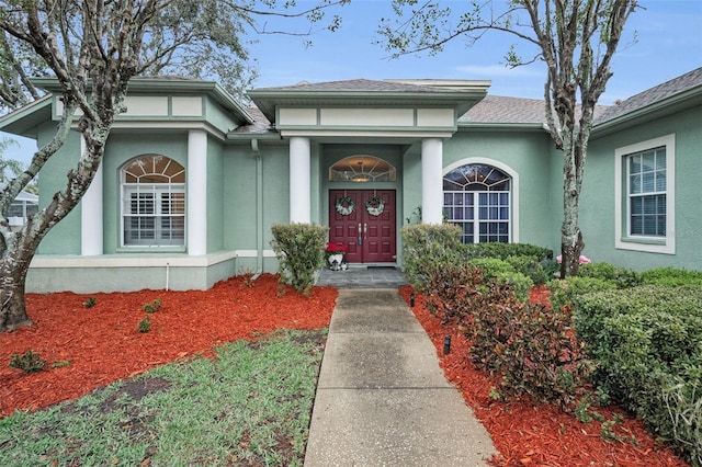 view of exterior entry featuring a shingled roof and stucco siding