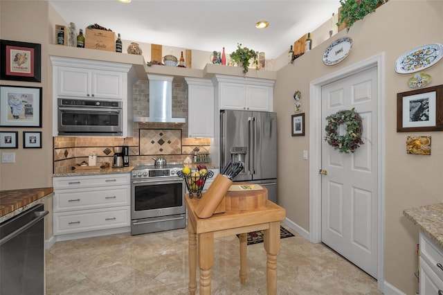 kitchen with wall chimney exhaust hood, appliances with stainless steel finishes, white cabinetry, and tasteful backsplash