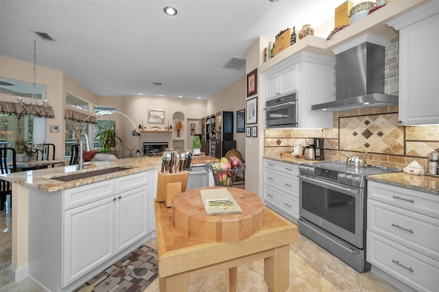 kitchen with a fireplace, stainless steel appliances, visible vents, a sink, and wall chimney range hood