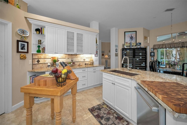 kitchen with backsplash, white cabinets, a sink, light stone countertops, and dishwasher