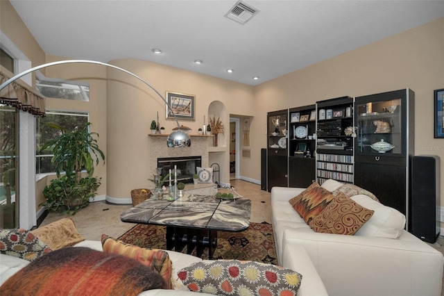 living room featuring arched walkways, recessed lighting, visible vents, a glass covered fireplace, and baseboards