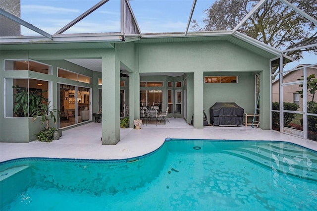 exterior space with an outdoor pool, glass enclosure, a patio area, and stucco siding