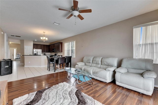 living room featuring ceiling fan with notable chandelier and light hardwood / wood-style floors