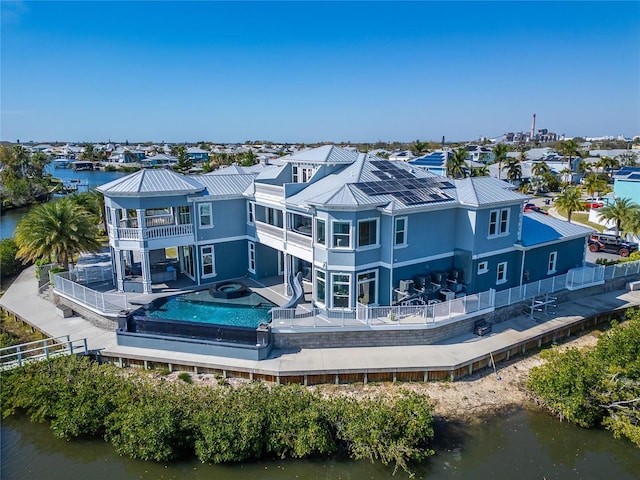 rear view of house with a fenced in pool, a water view, a hot tub, roof mounted solar panels, and a balcony