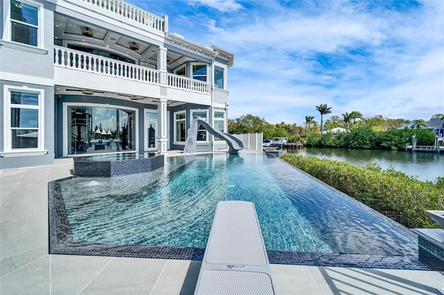 view of pool featuring a water view, a ceiling fan, a diving board, an infinity pool, and a patio area