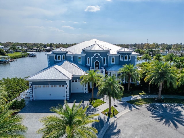 view of front facade featuring decorative driveway, a water view, an attached garage, a standing seam roof, and metal roof