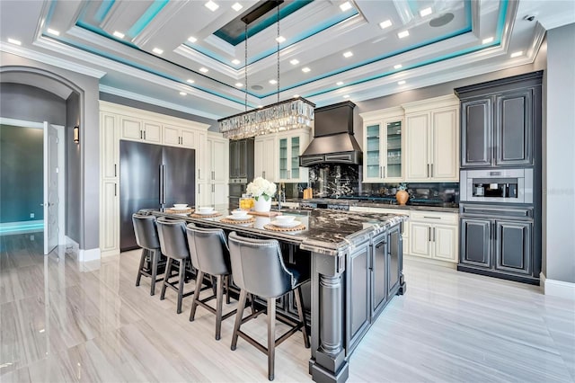 kitchen with a tray ceiling, arched walkways, custom exhaust hood, a breakfast bar area, and stainless steel appliances