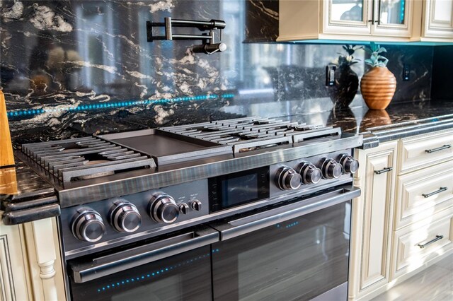 interior details with high end stainless steel range oven, tasteful backsplash, and cream cabinetry