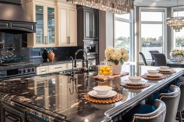 kitchen with wall chimney range hood, glass insert cabinets, backsplash, and cream cabinetry