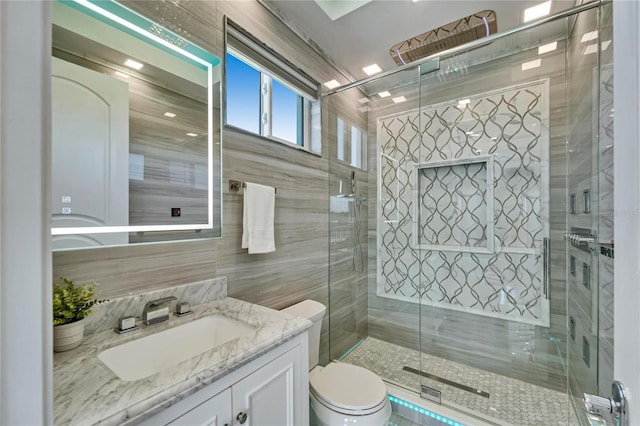 bathroom with tile walls, vanity, toilet, and a shower stall