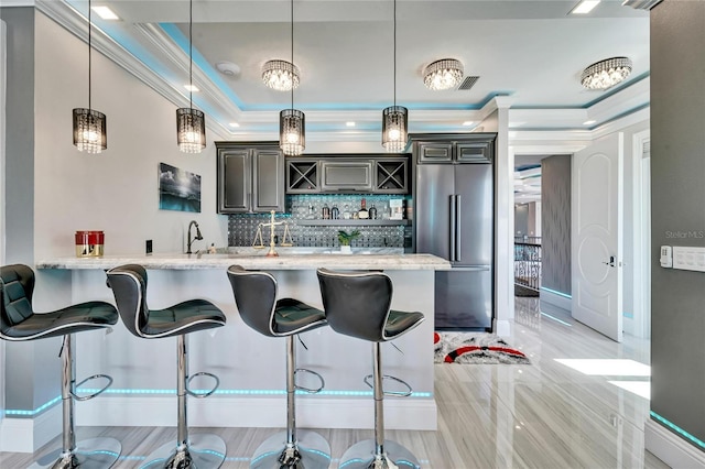 kitchen with stainless steel built in refrigerator, a raised ceiling, crown molding, and a kitchen breakfast bar