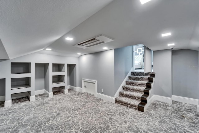 finished basement with a textured ceiling, stairs, baseboards, and built in features