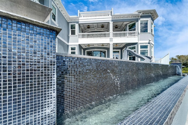 view of side of home with a ceiling fan, fence, a balcony, and stucco siding