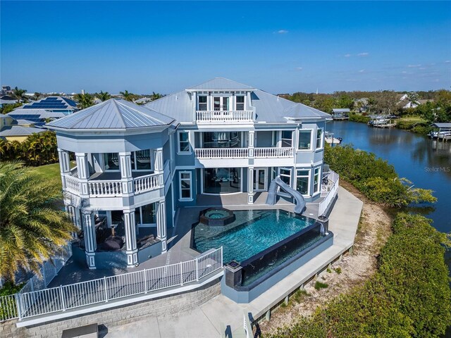 back of property featuring a patio, a balcony, metal roof, an in ground hot tub, and a water view