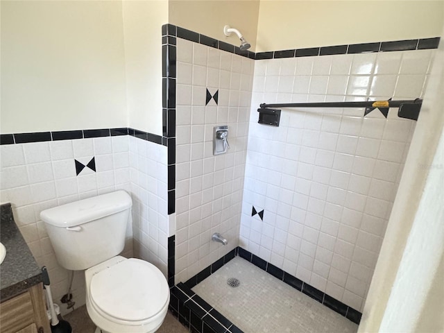 bathroom with vanity, tiled shower, tile walls, and toilet