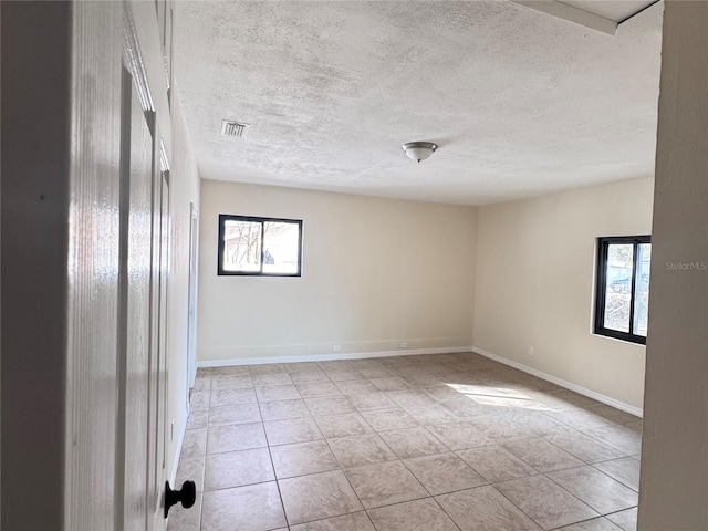 empty room featuring light tile patterned floors, a textured ceiling, and a wealth of natural light