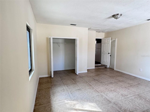 unfurnished bedroom featuring a closet, stainless steel refrigerator, and a textured ceiling